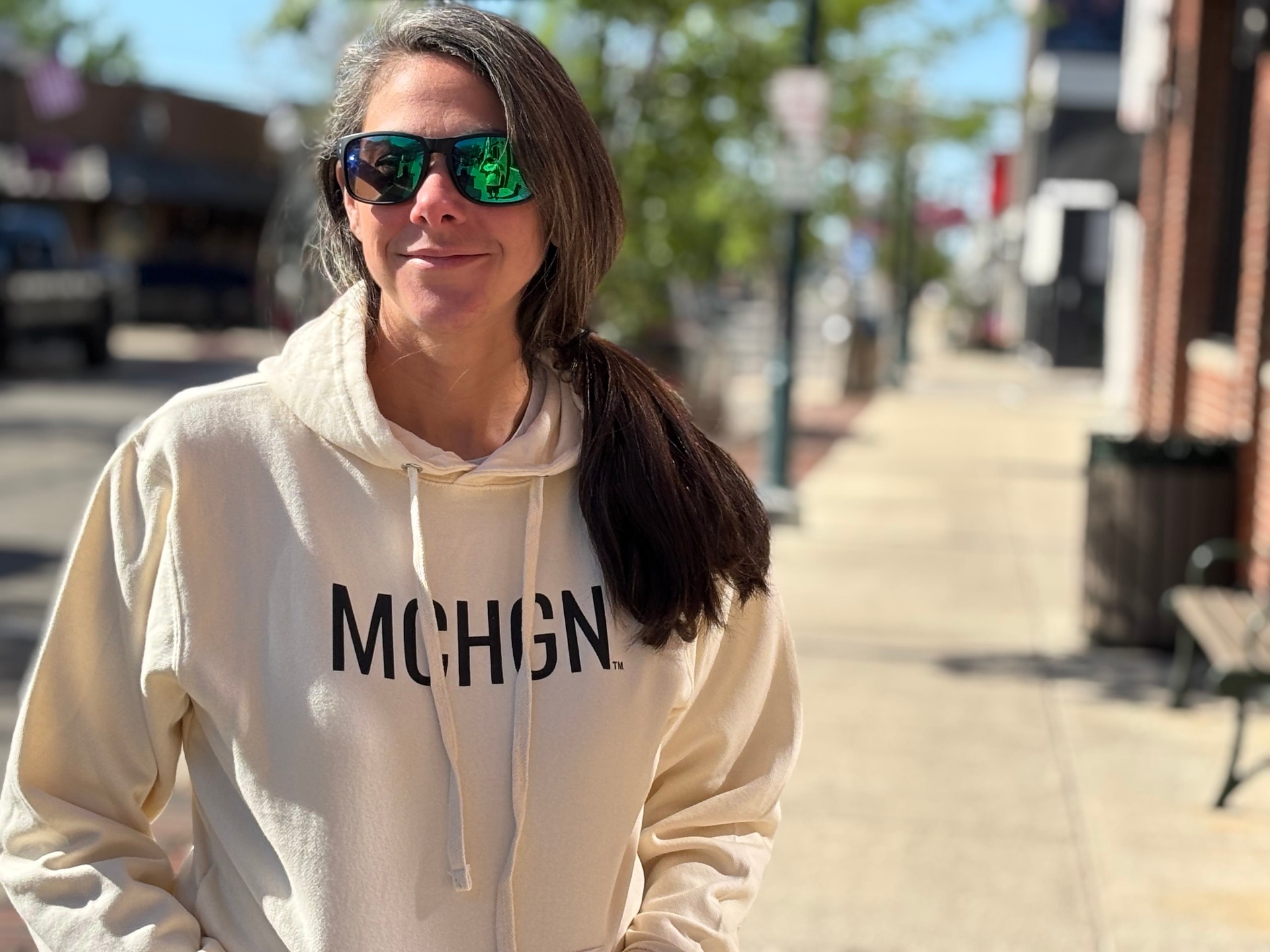 Woman wearing a cream MCHGN hoodie with the MCHGN wordmark on the chest